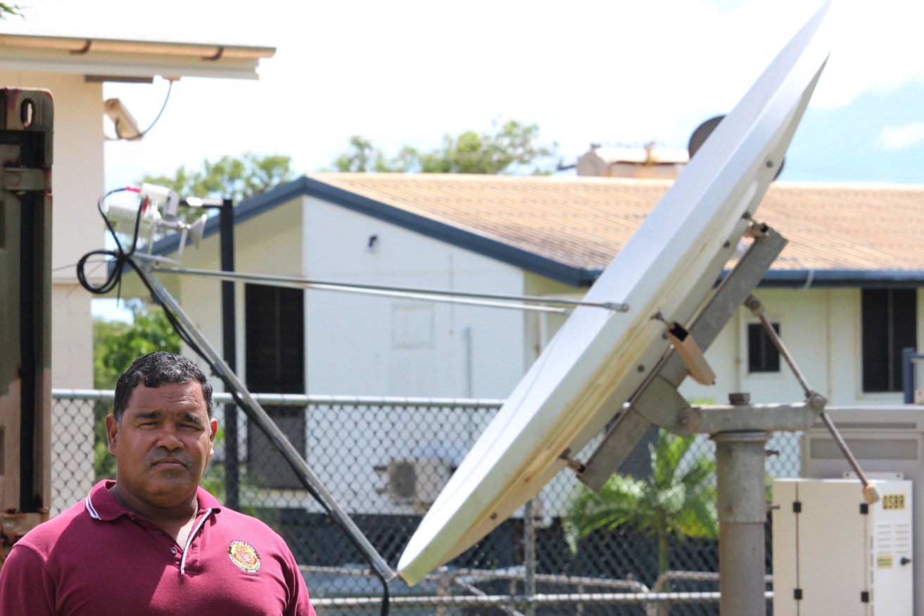 A supplied image obtained Tuesday, March 27, 2018 of Lockhart River mayor Wayne Butcher standing next to a temporary satellite dish brought in as an interim measure after phone services in the area were cut by a lightning strike six weeks ago in Lockhart River, Monday, March, 26, 2018. (AAP Image Supplied by Wayne Butcher, Christine Howes) NO ARCHIVING, EDITORIAL USE ONLY
